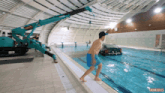 a shirtless man in blue shorts is walking into a swimming pool with a crane in the background that says thinkiules