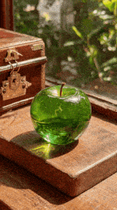 a green glass apple sits on a wooden table next to a window