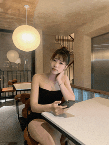a woman sits at a table with her hand on her chin looking at her phone
