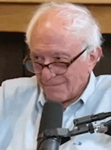 a man wearing glasses and a blue shirt is sitting in front of a microphone .