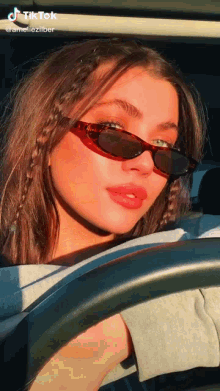 a woman wearing sunglasses and braids is driving a car .