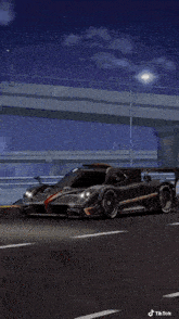 a black sports car is driving down a highway under a bridge .