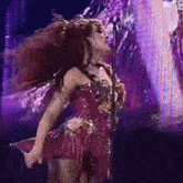 a woman in a red dress is singing into a microphone while her hair blows in the wind .