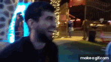 a man with a beard is laughing in front of a ferris wheel at night .