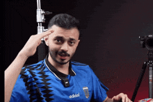 a man wearing a blue adidas shirt is pointing to his head