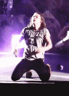 a man with long hair is kneeling down on a stage with purple lights behind him