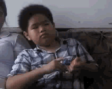 a young boy in a plaid shirt is sitting on a couch and playing with a toy .