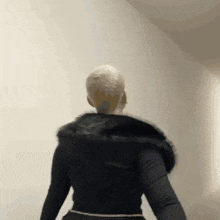a woman wearing a black fur coat is standing in front of a wall .