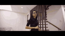 a woman wearing glasses is standing in front of a staircase