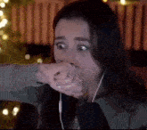 a woman wearing headphones is covering her mouth with her fist .