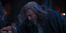 a man with long hair and a beard is standing in a dark room with the words pranay varma below him