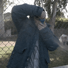 a man in a blue jacket is holding a can of soda in front of a chain link fence