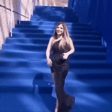 a woman in a black dress is standing on a blue carpet .