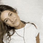 a woman wearing a white shirt and a silver chain necklace smiles for the camera