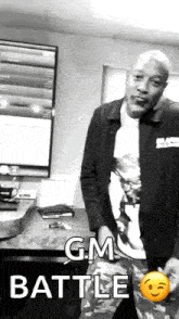 a man in a black jacket is standing in front of a desk with the words " gm battle " on it