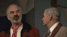 a man with a beard and a scarf around his neck talks to another man