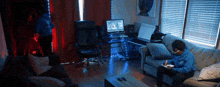 a man in a blue sweatshirt sits on a couch in front of a keyboard