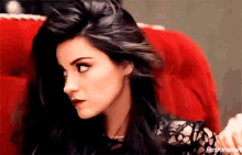 a woman with long black hair is sitting in a red chair and looking at the camera .