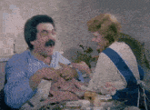 a man and a woman are sitting at a table and the man is holding something in his hand