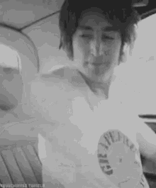 a black and white photo of a man in a white shirt taking a selfie in a car .