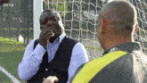 two men are talking in front of a soccer net with the bbc logo on the bottom
