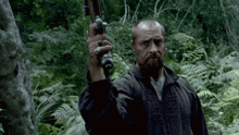 a man with a beard holds a gun in a forest