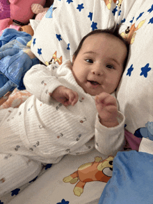 a baby is smiling while laying on a bed with a pillow that has blue flowers on it