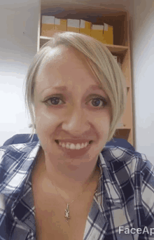 a woman wearing a plaid shirt and a necklace smiles in front of a shelf with yellow folders