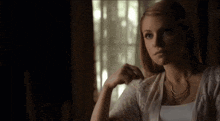 a woman wearing a white sweater and a necklace looks out a window