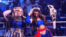 two women are standing in a wrestling ring and one has a championship belt