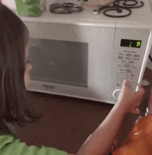 a child is holding a remote control in front of a microwave with the number 9 on the screen