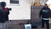 a man wearing a black no2 hoodie is standing in front of a house