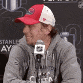 a man wearing a red and white hat and a gray hoodie is sitting in front of a microphone .