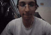 a man wearing glasses and a white t-shirt looks at the camera