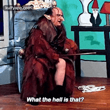 a man in a costume is sitting in a chair with a cane and says `` what the hell is that '' .