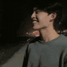 a young man in a grey shirt is smiling in front of a beach at night