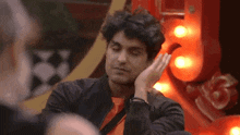a man sitting in front of a red sign with his hand on his forehead
