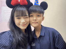 a girl wearing mickey mouse ears stands next to a boy wearing a wizard hat