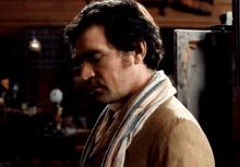 a man with a scarf around his neck looks down at something