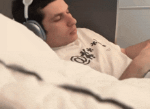 a man wearing headphones is laying on a bed with his eyes closed and a shirt that says o on it