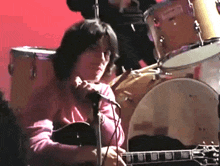 a man is playing a guitar and singing into a microphone in front of a drum set