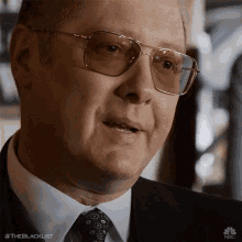 a close up of a man wearing glasses and a suit with the hashtag #theblacklist