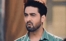 a man with a beard is wearing a green shirt and making a face .
