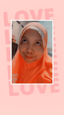 a girl wearing an orange hijab looks up at the word love on a pink background