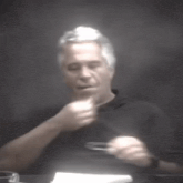 a man in a black shirt is sitting at a table with a piece of paper in front of him