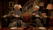 two older men sit on a couch holding cups of tea with the words i 'm visible in pink