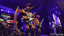 a man in a robot costume is playing a guitar in front of a large screen that says gifrun.com