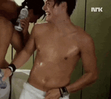 a shirtless man with a towel around his waist is standing next to another shirtless man holding a bottle of water .