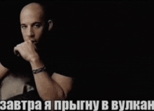 a bald man with a bracelet on his wrist is sitting in a dark room with a caption in russian