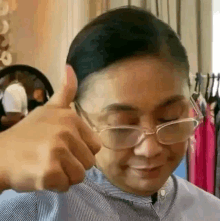 a woman wearing glasses is giving a thumbs up in a store .